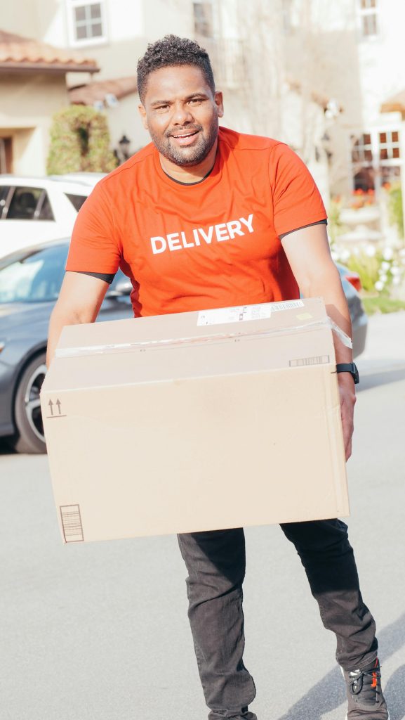 African American delivery man holding a cardboard box in a residential area, smiling.